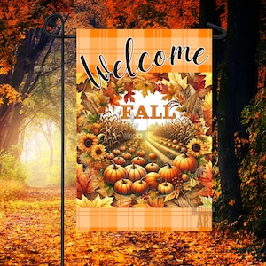 Puede incluir: Una bandera de jardín de otoño con un fondo de cuadros naranja y blanco. La bandera presenta una corona de hojas de otoño con la palabra "otoño" en el centro. La corona rodea un camino bordeado de calabazas y tallos de maíz.