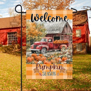 May include: A garden flag with a fall theme. The flag features a red vintage truck filled with pumpkins, parked in front of a barn. The words "Welcome Pumpkin Season" are displayed on the flag.