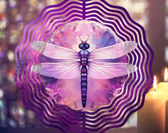 May include: A decorative dragonfly wind spinner in shades of purple and lavender. The dragonfly has detailed wings and body, set against a floral background. The spinner is framed by a wavy, gold-trimmed border and hangs from a chain.