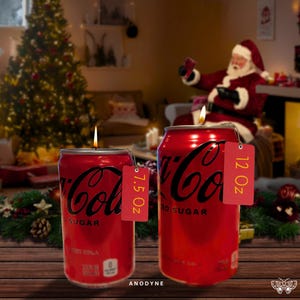 May include: Two red Coca-Cola can candles with black lettering. The smaller candle is labeled "7.5 OZ" and the larger candle is labeled "12 OZ". Both candles have a flame on top.