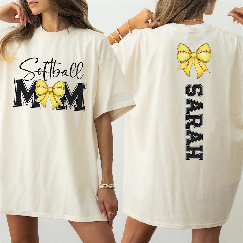 A woman wearing a white t-shirt with the text "Softball Mom" and a yellow bow on the back.