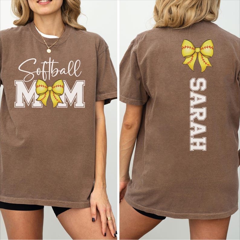 A woman wearing a brown t-shirt with the text "Softball Mom" and a yellow bow on the back.