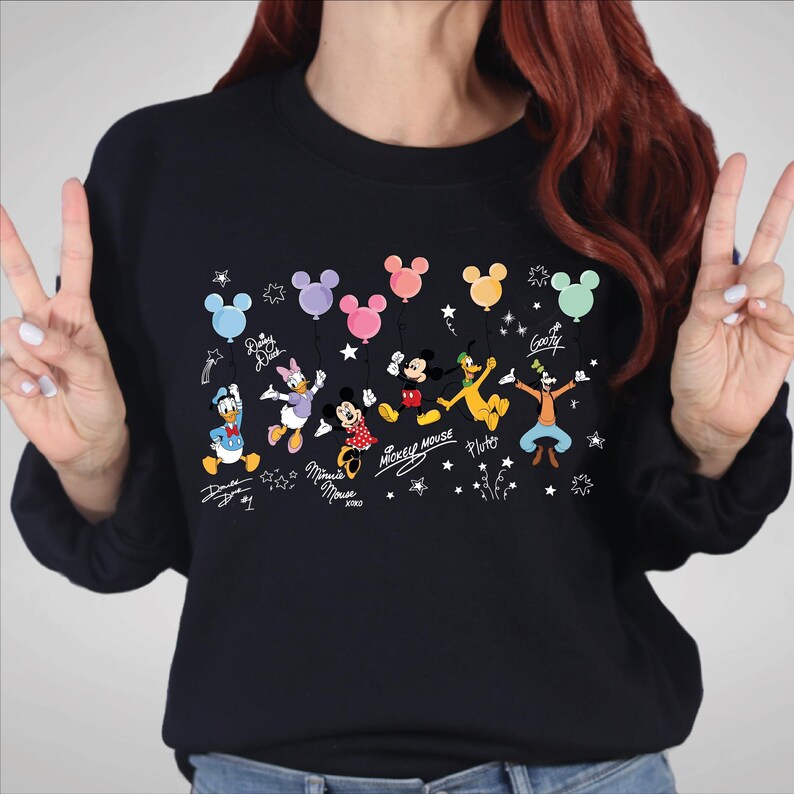 A woman wearing a black sweater with a graphic design featuring various Disney characters and balloons.