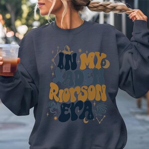 a woman holding a drink and wearing a sweatshirt