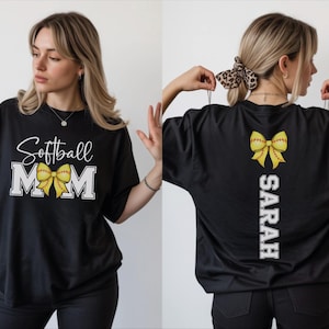 A woman wearing a black t-shirt with a white text design and a yellow bow on the back.