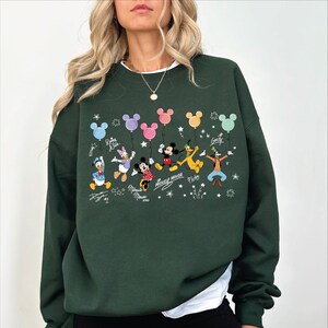 A woman wearing a green sweatshirt with a Disney character design on it.