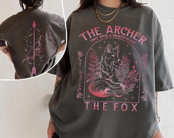 May include: Dark gray t-shirt with a pink graphic of a fox inside an archway, with text that reads "THE ARCHER" and "THE FOX". The back of the shirt features a pink arrow and bow design.