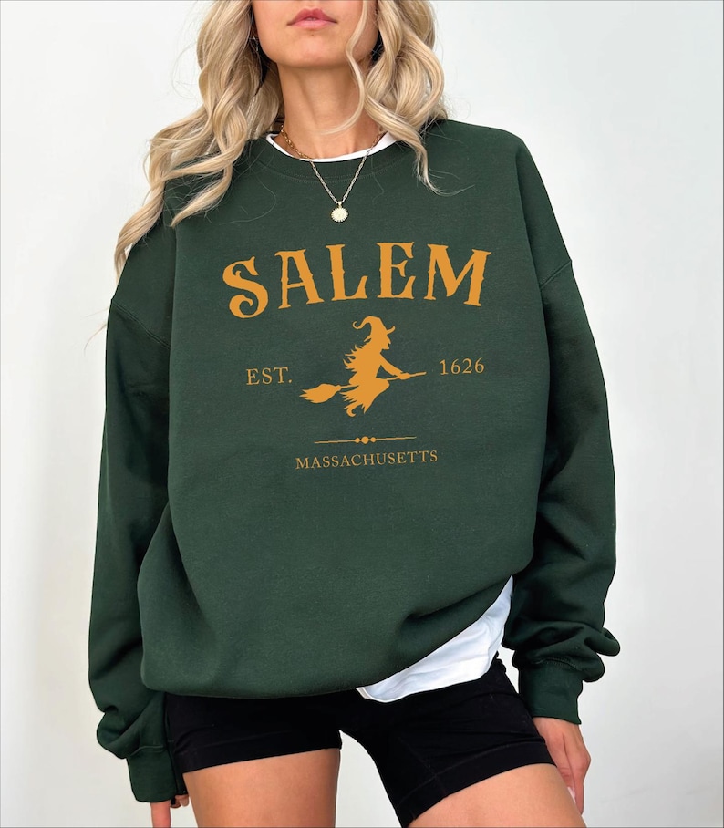 A woman wearing a green sweatshirt with the text "SALEM EST. 1626 MASSACHUSETTS" printed on it.