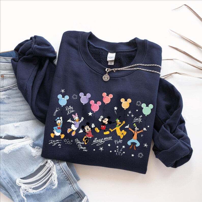 A navy blue sweatshirt with a Disney character design, including Mickey Mouse, Donald Duck, Goofy, and Pluto, along with various Disney-themed elements such as balloons and stars.