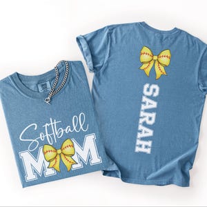 A blue t-shirt with a yellow bow and the text "Softball Mom" printed on it, along with a name tag that reads "SARAH".