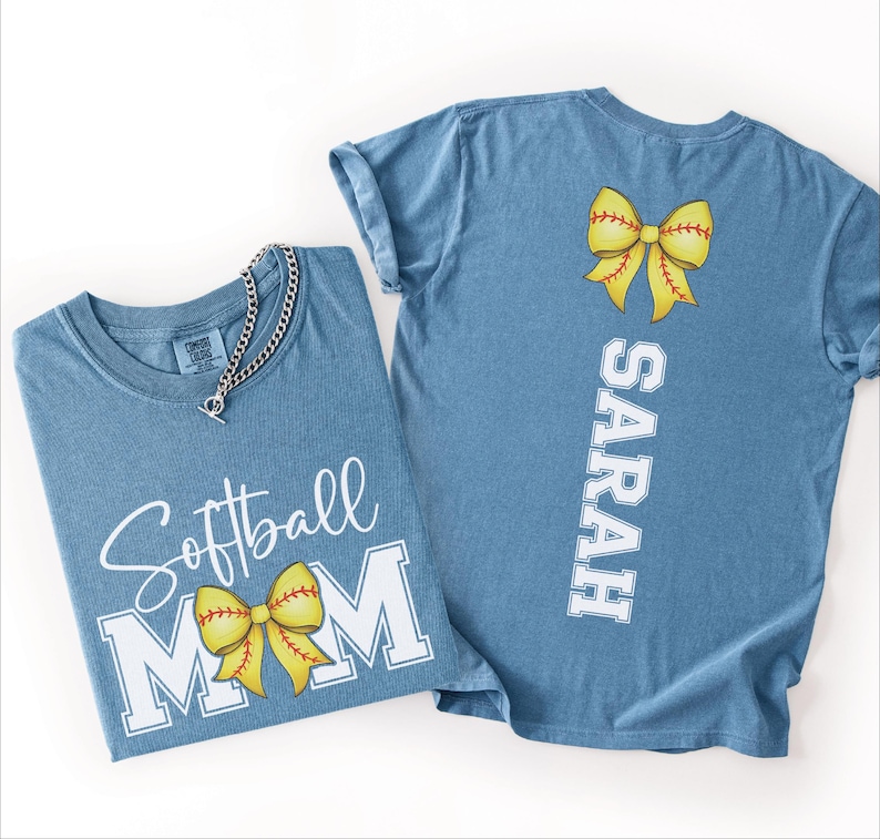 A blue t-shirt with a yellow bow and the text "Softball Mom" printed on it, along with a name tag that reads "SARAH".