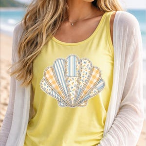 May include: Yellow tank top featuring a seashell design. The seashell is made of various fabric patterns, including blue and white stripes, yellow gingham, and floral prints. The tank top is worn with a white cardigan.