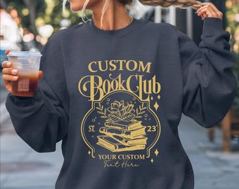 May include: A dark blue sweatshirt with a gold graphic design that says "Custom Book Club" with a stack of books, a flower, and the text "Your Custom Text Here".