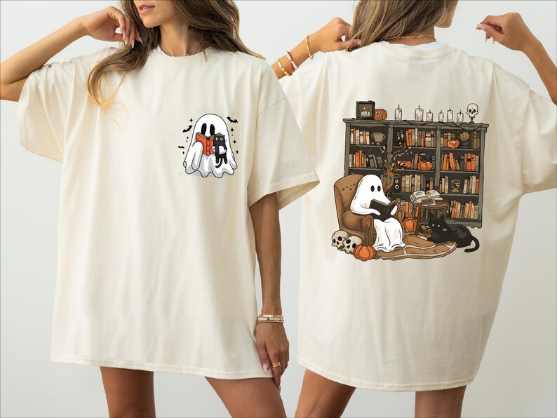 two women wearing white t-shirts with Halloween-themed designs. The t-shirt on the left features a ghost and a witch, while the t-shirt on the right depicts a ghost reading a book and a cat.