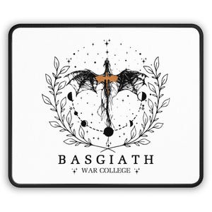 May include: A white mouse pad with a black and orange design. The design features a dragon with its wings spread, surrounded by a wreath of leaves and stars. The text "BASGIATH WAR COLLEGE" is printed below the design.