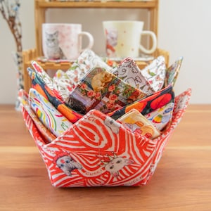 May include: A set of colorful fabric bowl cozies in a flower pattern. The cozies are folded into a flower shape and are made of a variety of fabrics, including floral prints, animal prints, and geometric patterns.