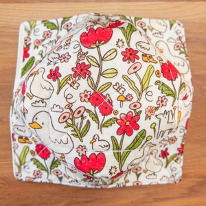 May include: A white quilted fabric bowl with a floral pattern featuring red, pink, and green flowers, white birds, and other small details. The bowl is ideal for serving snacks or holding small items.