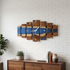 May include: A horizontal wall clock composed of seven vertical segments of natural wood with a continuous inlay of translucent blue resin running through the center. The clock features thin white hands and simple white markers on the face.