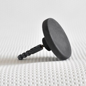 May include: A black plastic wall anchor with a round, flat head. The anchor is designed for use with drywall or plaster.