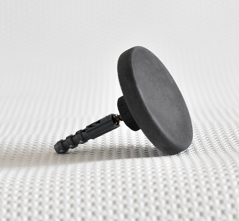 May include: A black plastic wall anchor with a round, flat head. The anchor is designed for use with drywall or plaster.