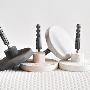 May include: Three concrete wall anchors with grey plastic anchors and screws. The anchors are round and have a flat surface.