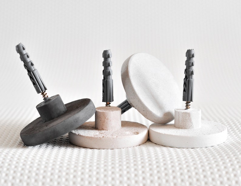 May include: Three concrete wall anchors with grey plastic anchors and screws. The anchors are round and have a flat surface.