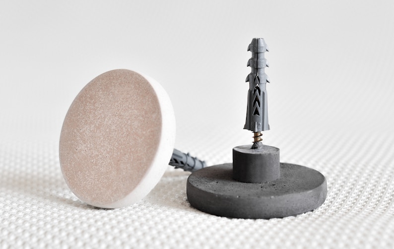 May include: Two concrete wall anchors with a grey plastic drywall anchor in the centre. The anchors are round and have a flat top. The drywall anchor is a standard size and has a screw in the centre.