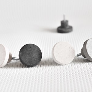 Op de afbeelding: Vijf ronde betonnen kastknoppen in twee kleuren: grijs en wit. De knoppen hebben een gespikkelde textuur en zijn in een rij gerangschikt.