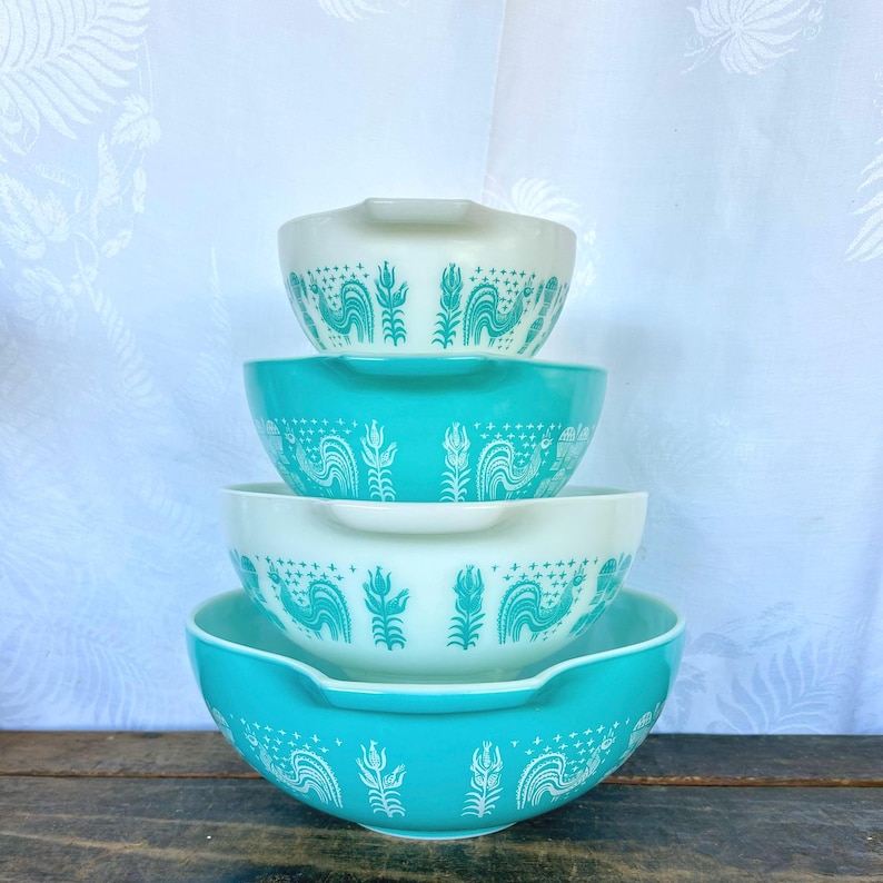 May include: Set of four nesting mixing bowls with a white background and a turquoise blue rooster design. The bowls are stacked in order of size, with the largest bowl on the bottom and the smallest bowl on top.
