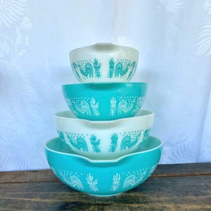 May include: Set of four turquoise and white mixing bowls with a rooster and floral design. The bowls are stacked on top of each other.