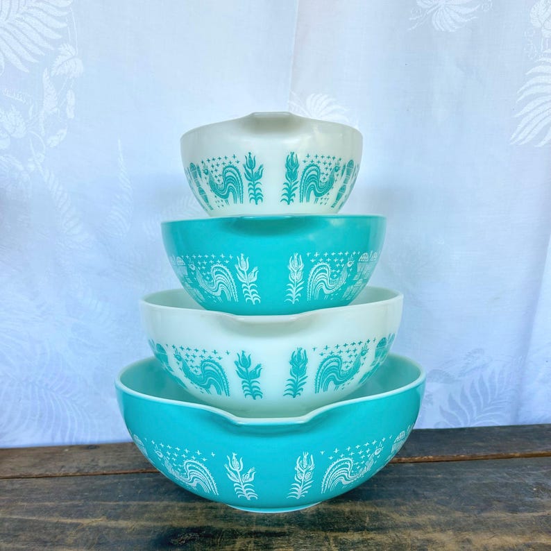 May include: Set of four turquoise and white mixing bowls with a rooster and floral design. The bowls are stacked on top of each other.