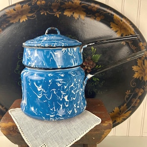 May include: A blue and white enamelware coffee pot with a lid, featuring a marbled pattern. The pot has a black handle and sits on a small wooden stool. A decorative tray with gold leaf accents is in the background.