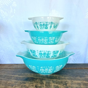 May include: Set of four turquoise and white mixing bowls with a vintage-inspired design featuring a repeating pattern of people and hot air balloons.