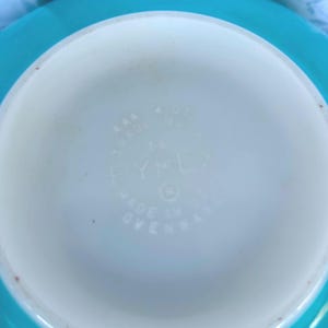 May include: Close-up of the bottom of a turquoise Pyrex bowl. The bowl is marked "Made in USA Ovenware" and has a Pyrex logo.