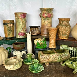 May include: A collection of ceramic vases, planters, and decorative items in various shapes and sizes. The items feature earthy tones of brown, green, and beige, with some pieces showcasing floral and nature-inspired designs. Includes a teapot, frog figurines, and a gourd-shaped vase.
