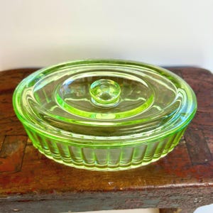 May include: A vintage green glass jar with a fluted lid. The jar has a clear glass lid with a knob on top.