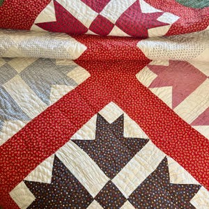 May include: A folded quilt with a patchwork design. The quilt features red, white, and blue fabrics. The design includes star and square patterns. The red fabric has a small floral print. The quilt is made of multiple layers of fabric and has a quilted texture.