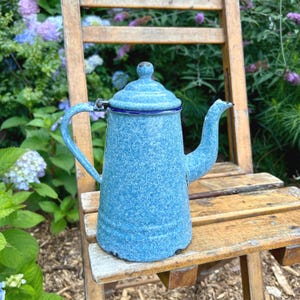 May include: A white ceramic mug with a black handle and the text "But First, Coffee" in a bold, black font. The mug is set against a blurred background, highlighting its clean design.