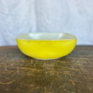 May include: A yellow glass mixing bowl with a white interior. The bowl is sitting on a wooden surface.