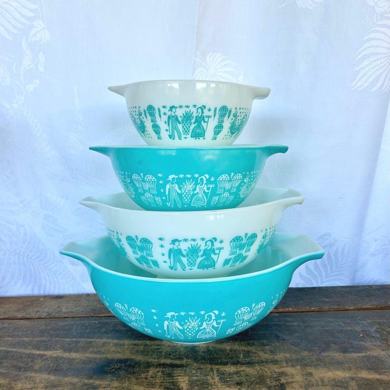 May include: Set of four turquoise and white mixing bowls with a folk art design. The bowls are nested inside each other.