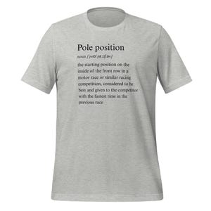 Puede incluir: Camiseta gris con la definición de "pole position" en texto negro. La definición explica que la pole position es la posición de salida en el interior de la primera fila en una carrera de motor o competición similar.