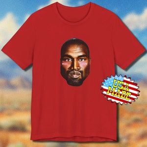 May include: Red t-shirt featuring a graphic of a man's face with blush on his cheeks. A star-shaped sticker with the text "USA MADE" is in the bottom right corner.