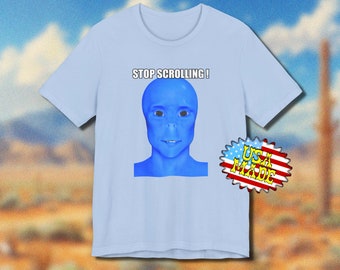 Pode incluir: Camiseta azul clara com um rosto alienígena azul e o texto "STOP SCROLLING!". A camiseta tem mangas curtas e gola redonda. Um adesivo "USA MADE" é visível no lado direito.