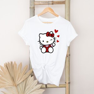 Op de afbeelding: Wit T-shirt met een rode Hello Kitty-afbeelding en rode hartjes. Het Hello Kitty-personage knippert met haar oog.