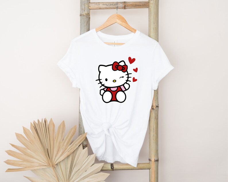 Op de afbeelding: Wit T-shirt met een rode Hello Kitty-afbeelding en rode hartjes. Het Hello Kitty-personage knippert met haar oog.