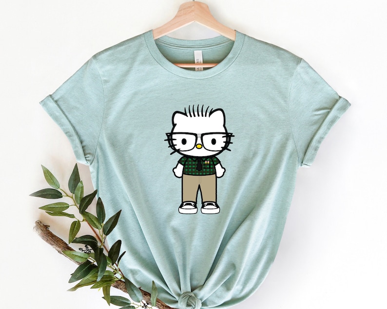 Puede incluir: Una camiseta azul claro con una imagen de dibujos animados de Hello Kitty con gafas y una camisa a cuadros.