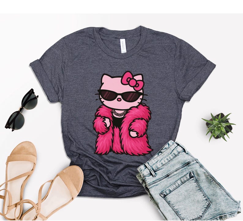 Puede incluir: Camiseta gris oscuro con un gato de dibujos animados que lleva gafas de sol y un abrigo de piel rosa. El gato tiene un lazo rosa y un collar. La camiseta se combina con pantalones cortos de mezclilla, gafas de sol y sandalias.