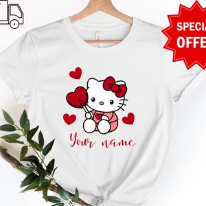 May include: White t-shirt with a cartoon image of Hello Kitty holding a red lollipop and surrounded by red hearts. The text "Your name" is printed below the image.