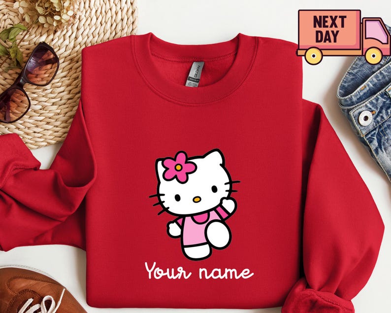 Puede incluir: Una sudadera roja con un personaje de dibujos animados con un vestido y una flor rosas. El texto "Your name" est&aacute; impreso en blanco. La sudadera tiene cuello redondo y mangas largas.