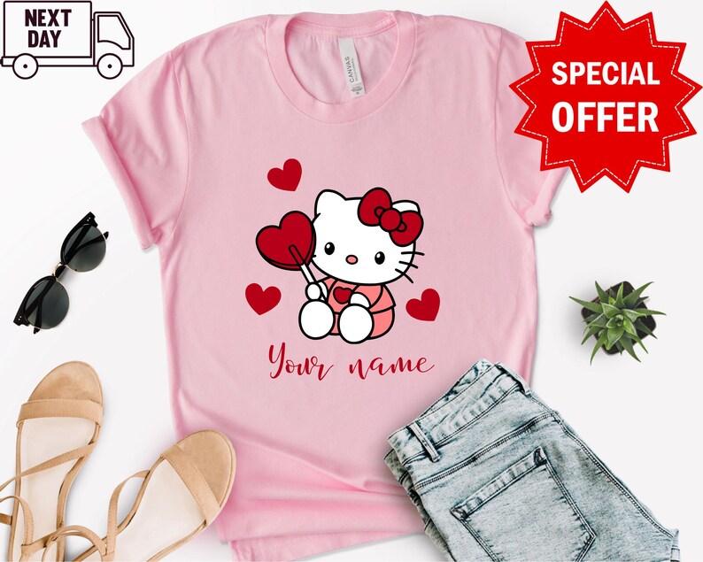May include: Pink t-shirt with a cartoon image of Hello Kitty holding a red heart-shaped lollipop. There are red hearts scattered around Hello Kitty. The text "Your name" is printed below Hello Kitty.
